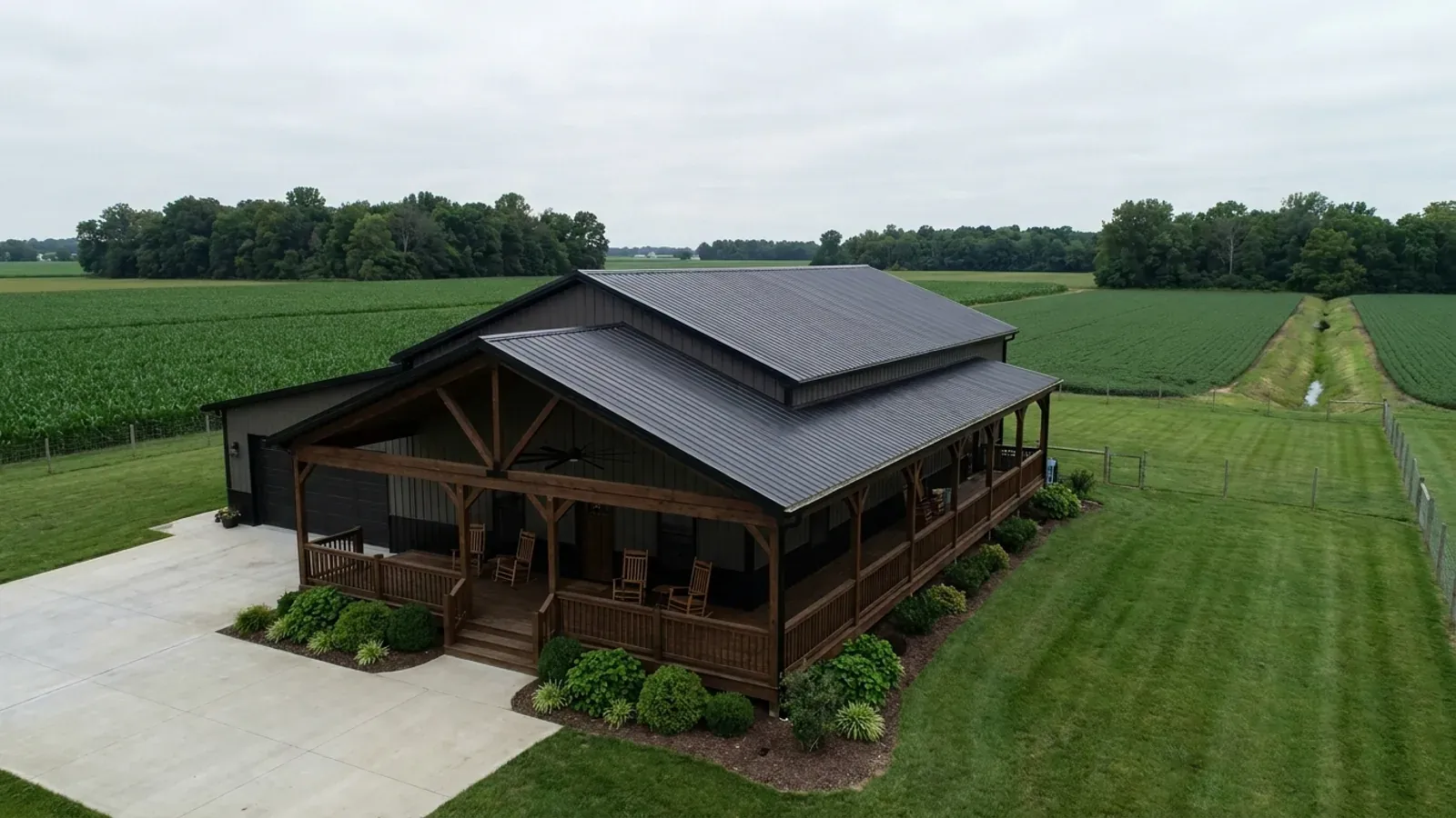 A barndominium exterior showing a deep wrap-around covered porch with posts and railing along two sides of the building.